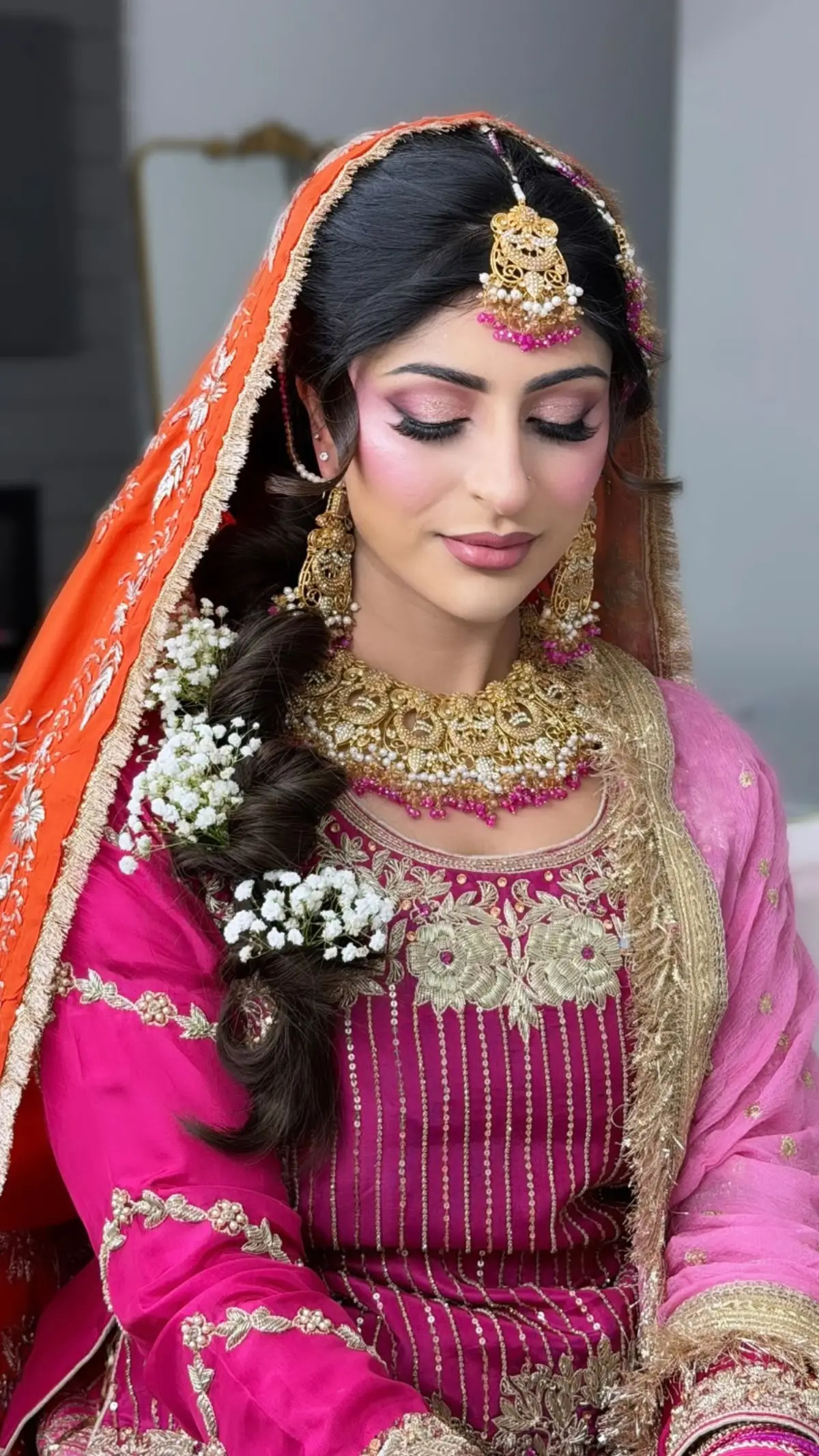 Bride in fuchsia with a coral dupatta over her head, a loose braid dressed with baby's breath.