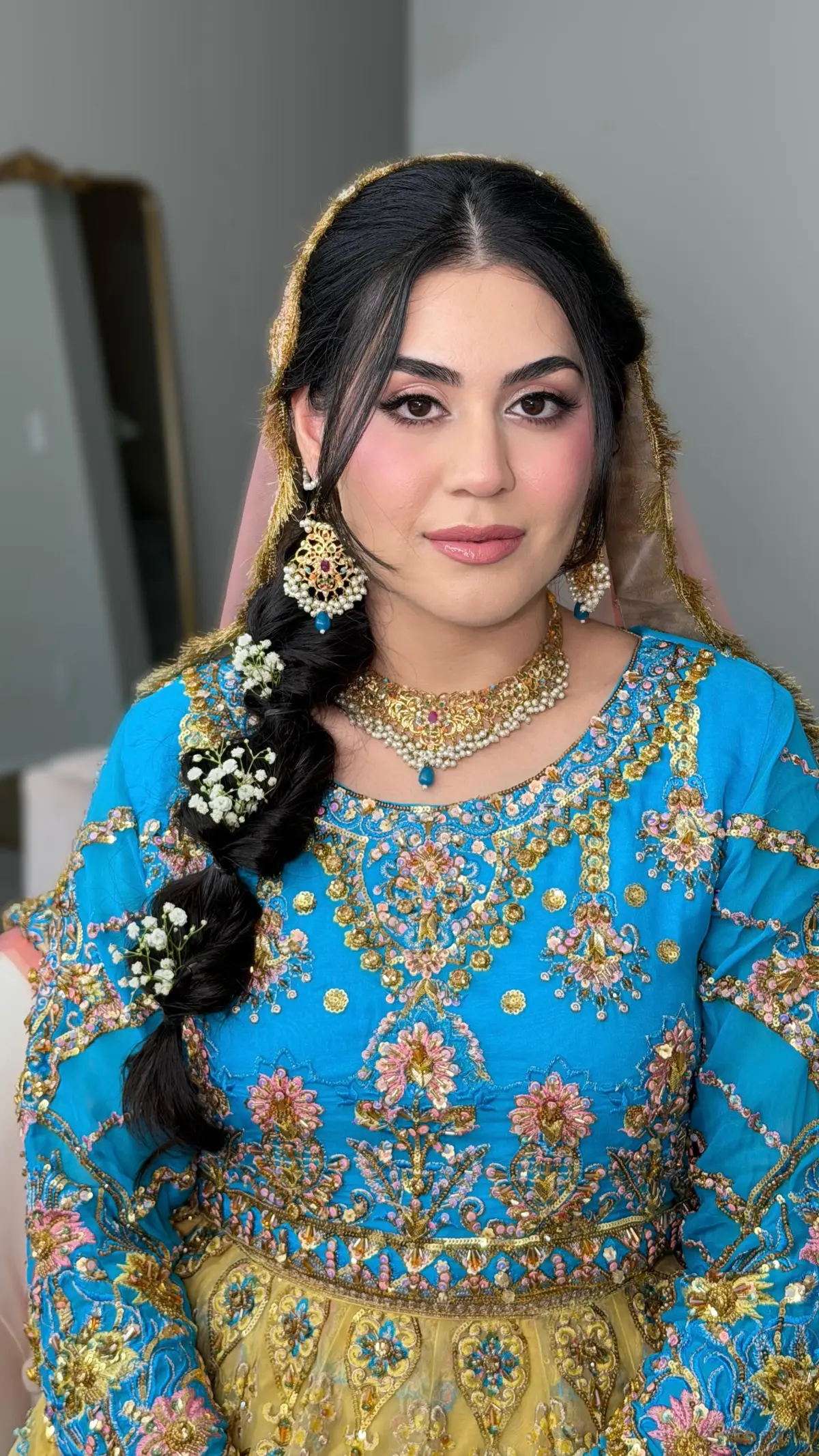 Bride in cobalt blue and gold with a side braid threaded with white flowers.