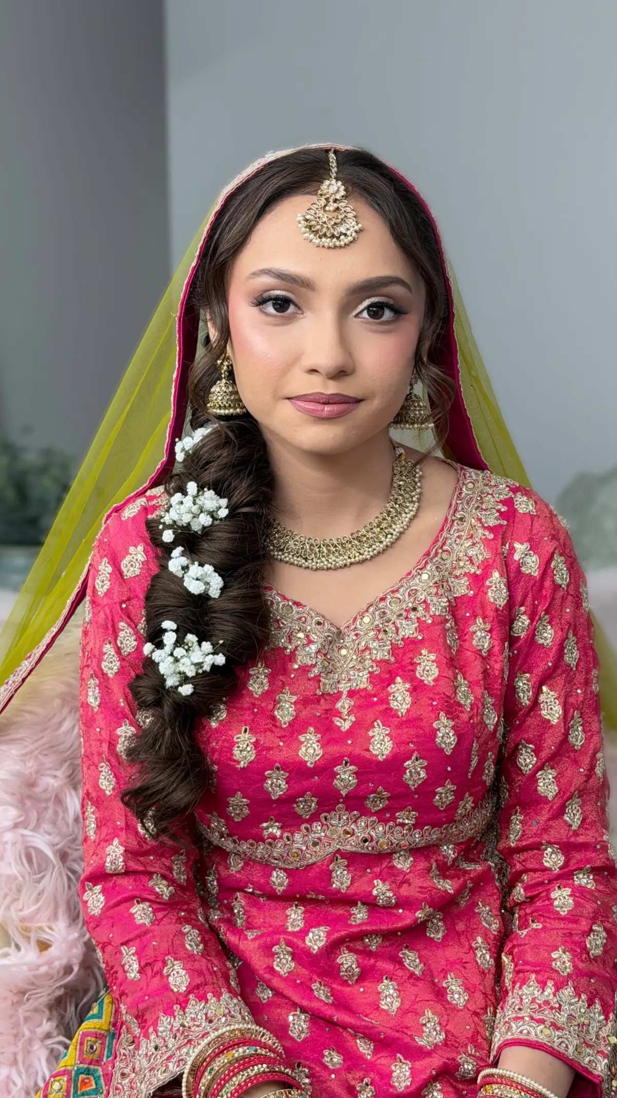 Bride in bright pink with a chartreuse dupatta and a flower-dressed braid over one shoulder.