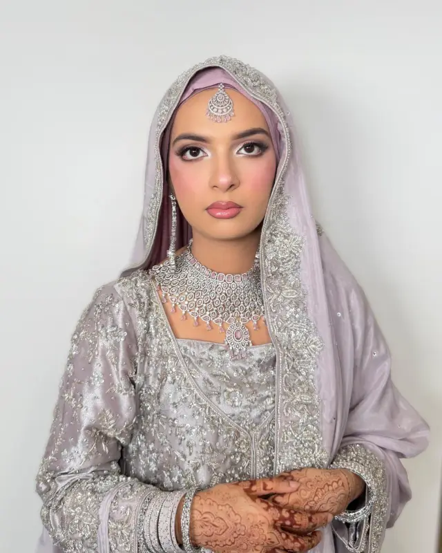 Hijabi bride in lilac and silver, hijab draped and pinned into a smooth crown, henna on her hands.