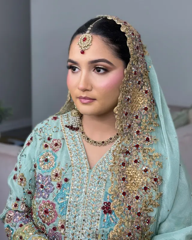 Bride in mint and gold with an embroidered dupatta draped over her head, maang tikka and soft rose makeup.
